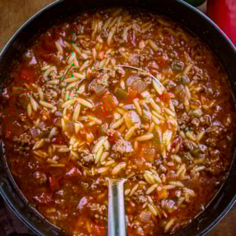 Ladle full of Stuffed Pepper Orzo Soup being held above the pot from overhead.