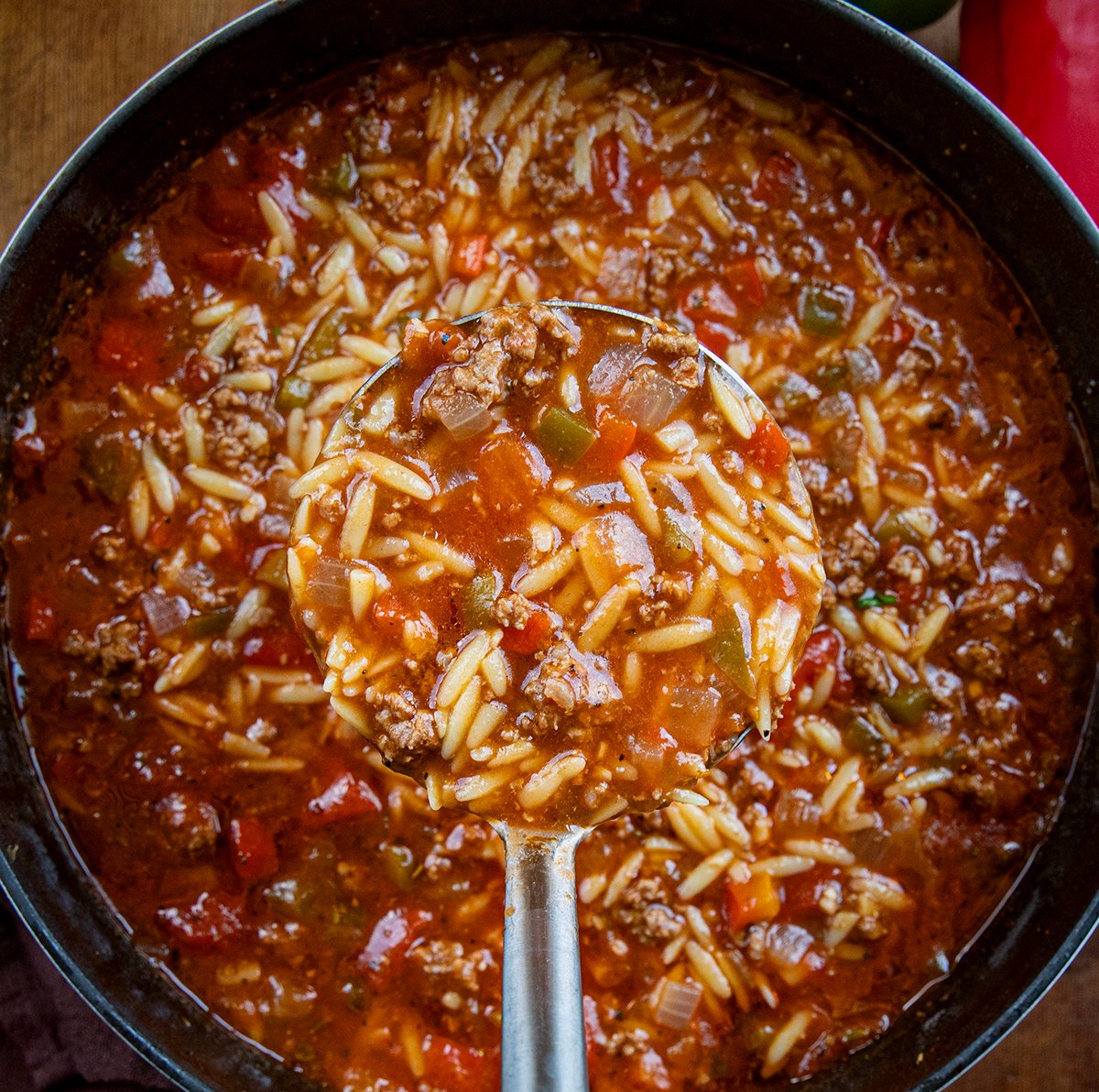 Ladle full of Stuffed Pepper Orzo Soup being held above the pot from overhead.