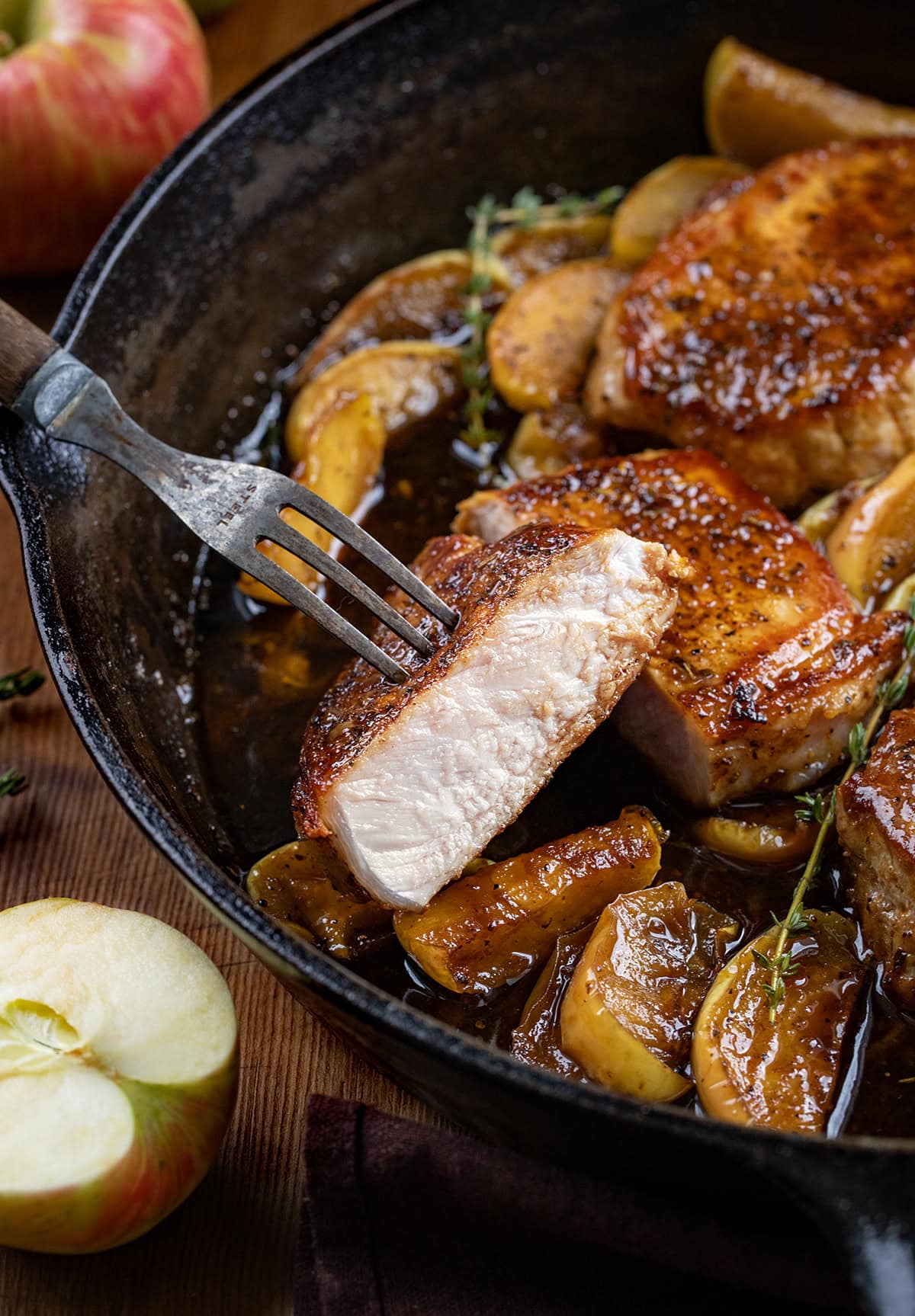 Fork holding a cut in half Apple Cider Pork Chop in the skillet.