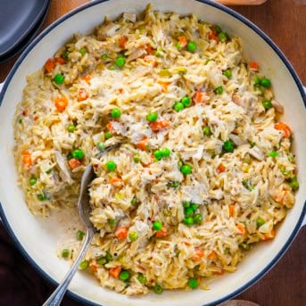 Spoon in a pan of Chicken Pot Pie Orzo on a wooden table from overhead.