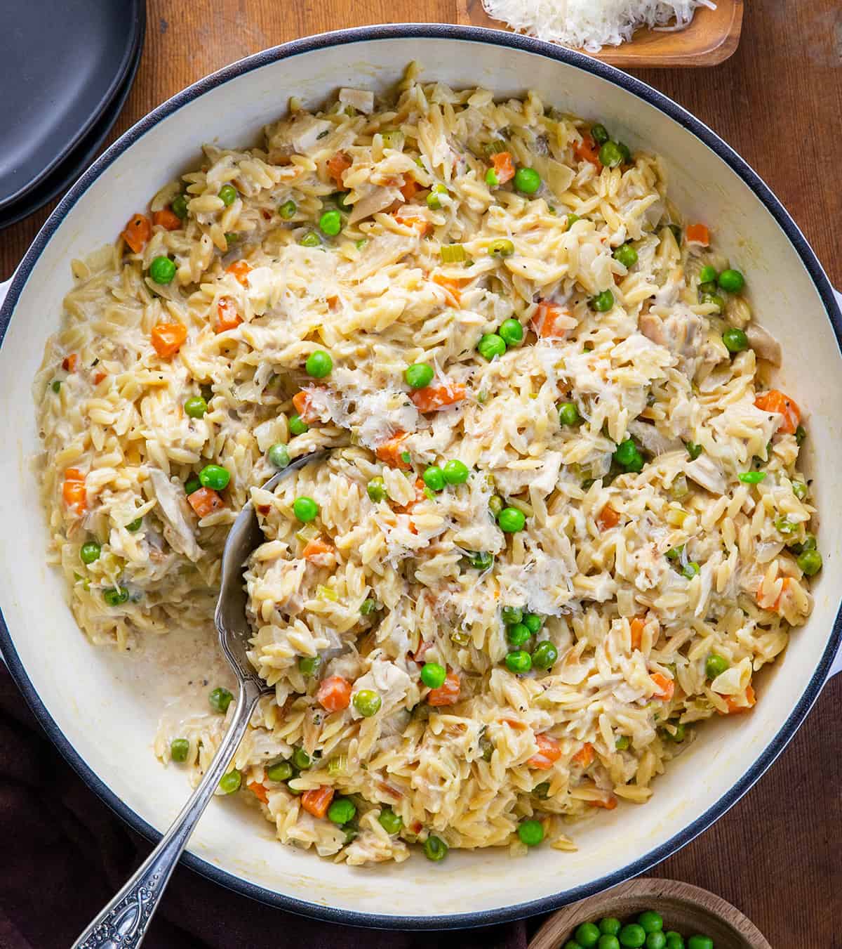 Spoon in a pan of Chicken Pot Pie Orzo on a wooden table from overhead. 