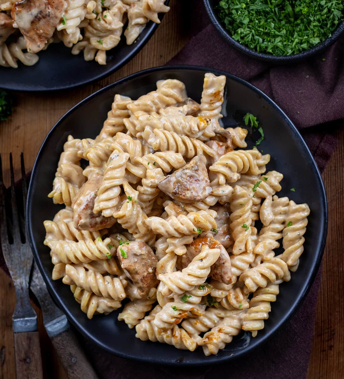 Black plates with Garlic Chicken Rotini on them on a wooden table from overhead.
