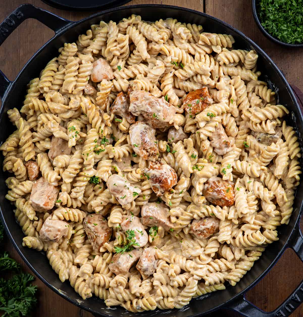 Skillet of mixed up Garlic Chicken Rotini on a wooden table from overhead.