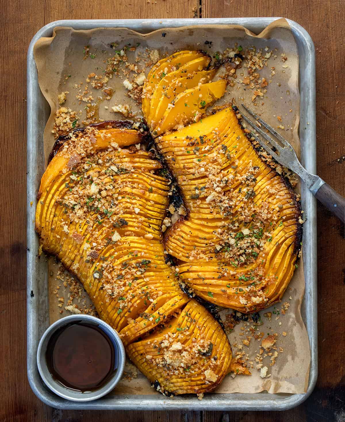 Hasselback Butternut Squash on a sheet pan on a wooden table from overhead.