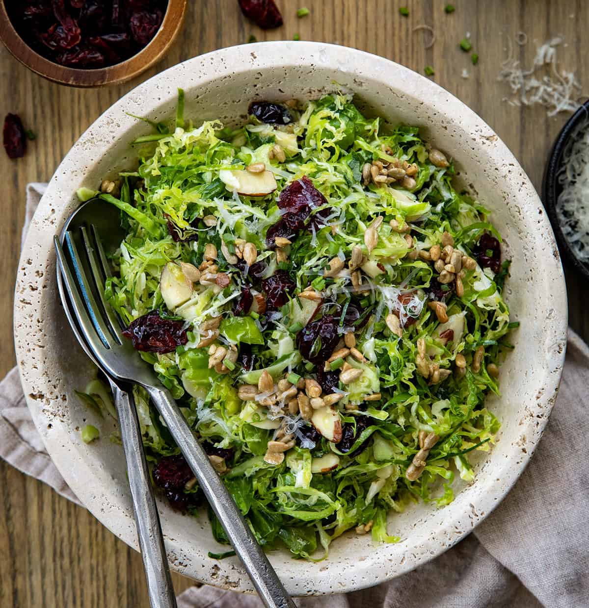 Bowl of Shaved Brussels Sprout Salad on a wooden table with serving spoons in it from overhead.