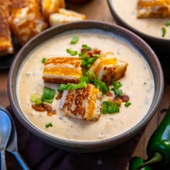 Bowls of Jalapeño Popper Soup on a wooden table with jalapenos.