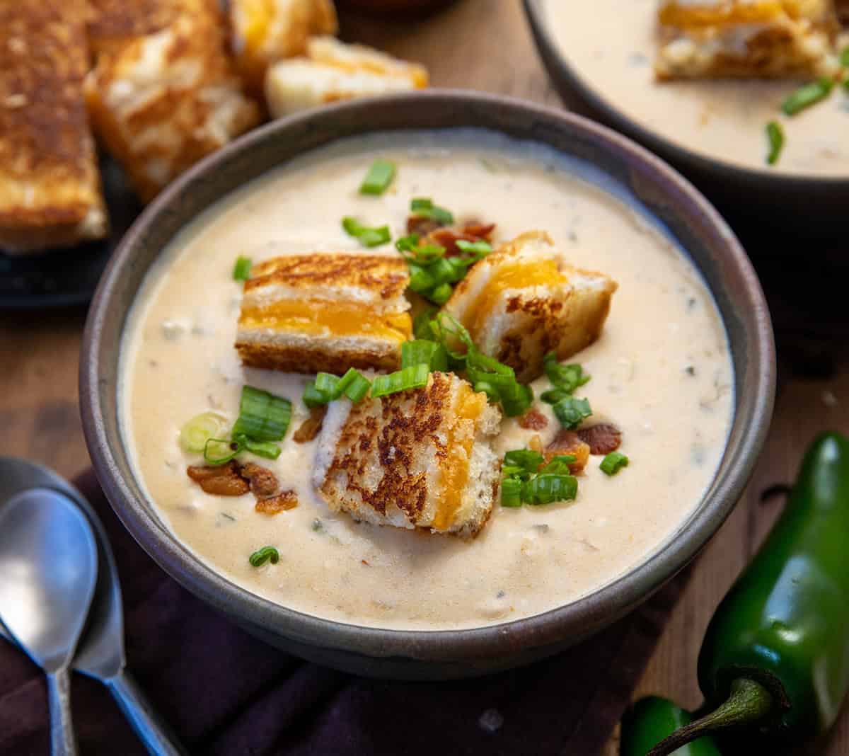 Bowls of Jalapeño Popper Soup on a wooden table with jalapenos.