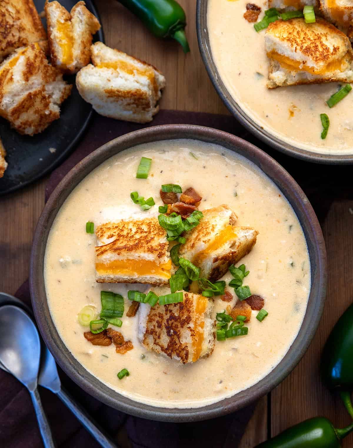 Bowls of Jalapeño Popper Soup on a wooden table with fresh jalapeno from overhead.