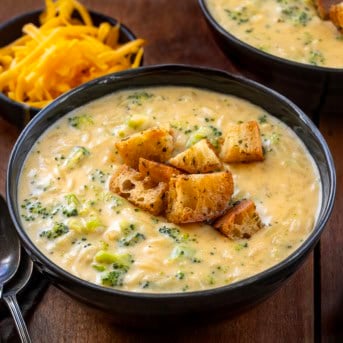 Black bowls of Broccoli Cheddar Orzo Soup on a wooden table.