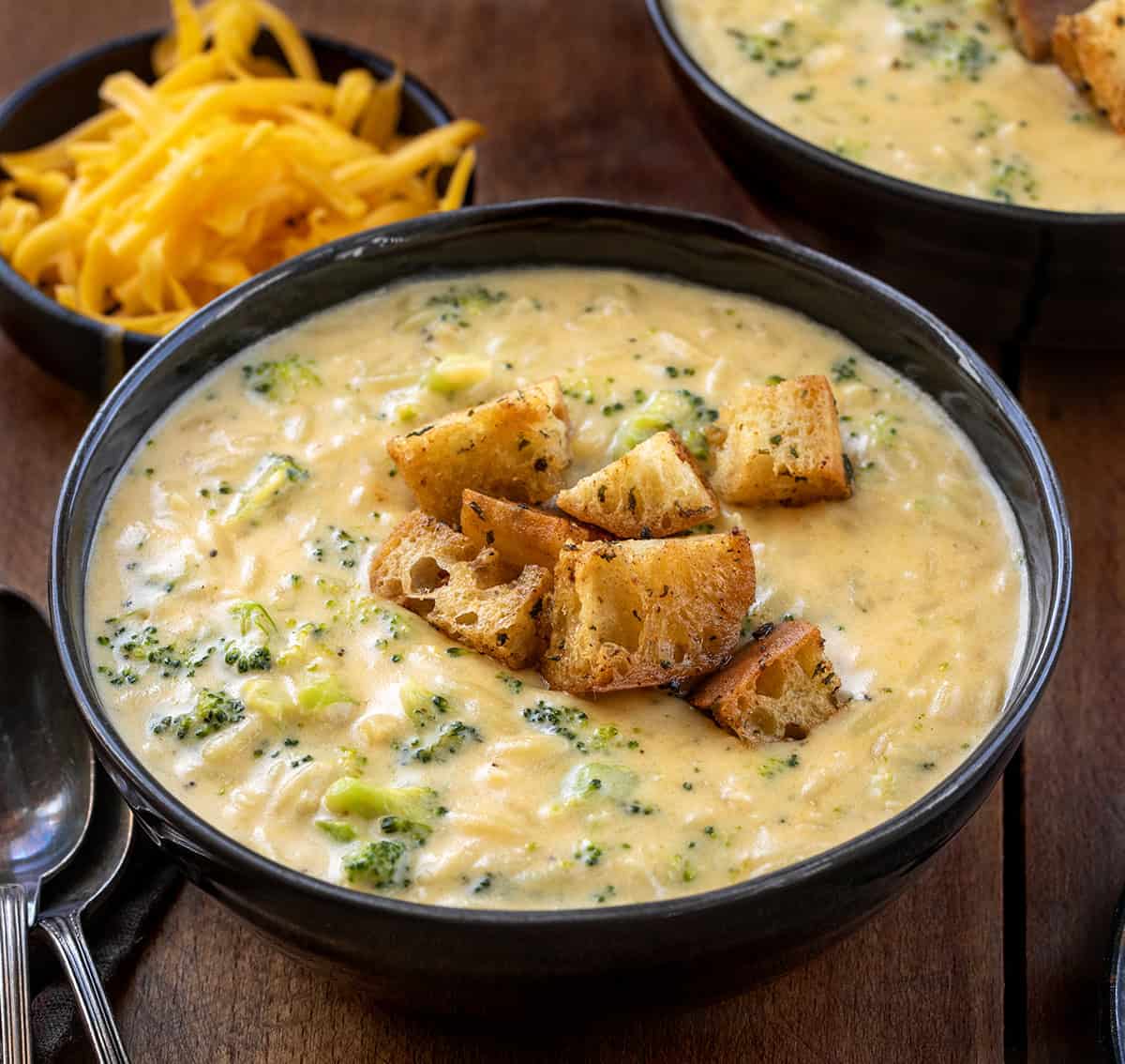 Black bowls of Broccoli Cheddar Orzo Soup on a wooden table.