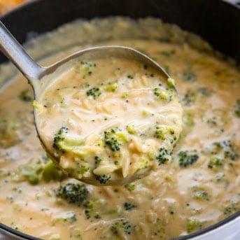 Ladle full of Broccoli Cheddar Orzo Soup held above the pot.
