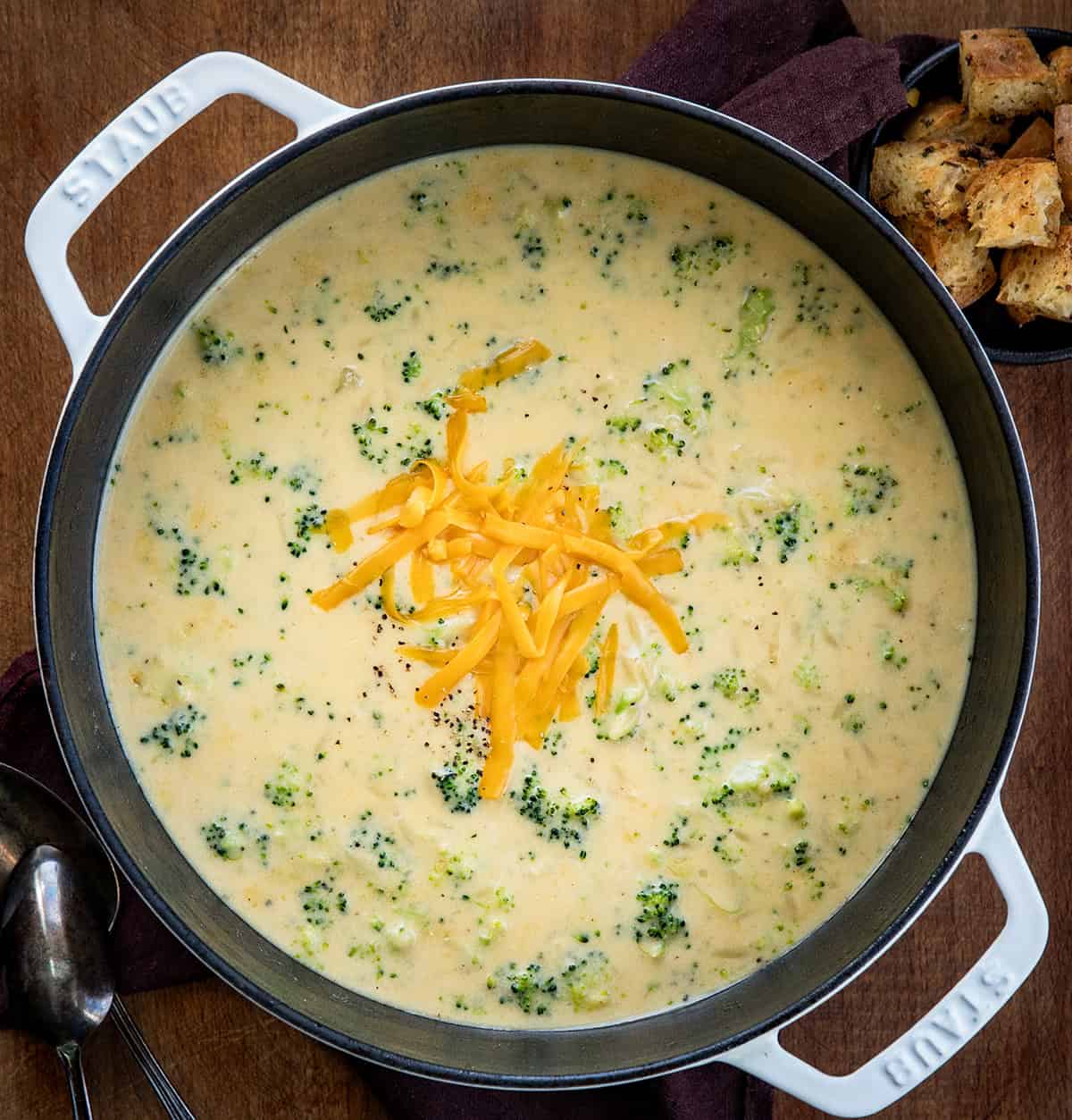 Pot of Broccoli Cheddar Orzo Soup on a wooden table with shredded cheddar cheese from overhead.