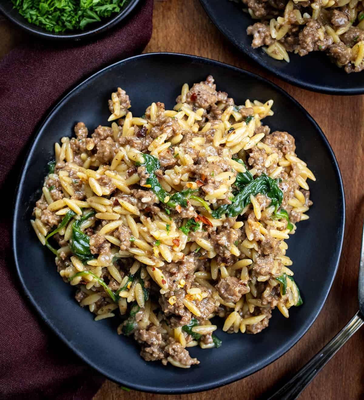 Black plates with Cheesy Beef Orzo on them on a wooden table from overhead.