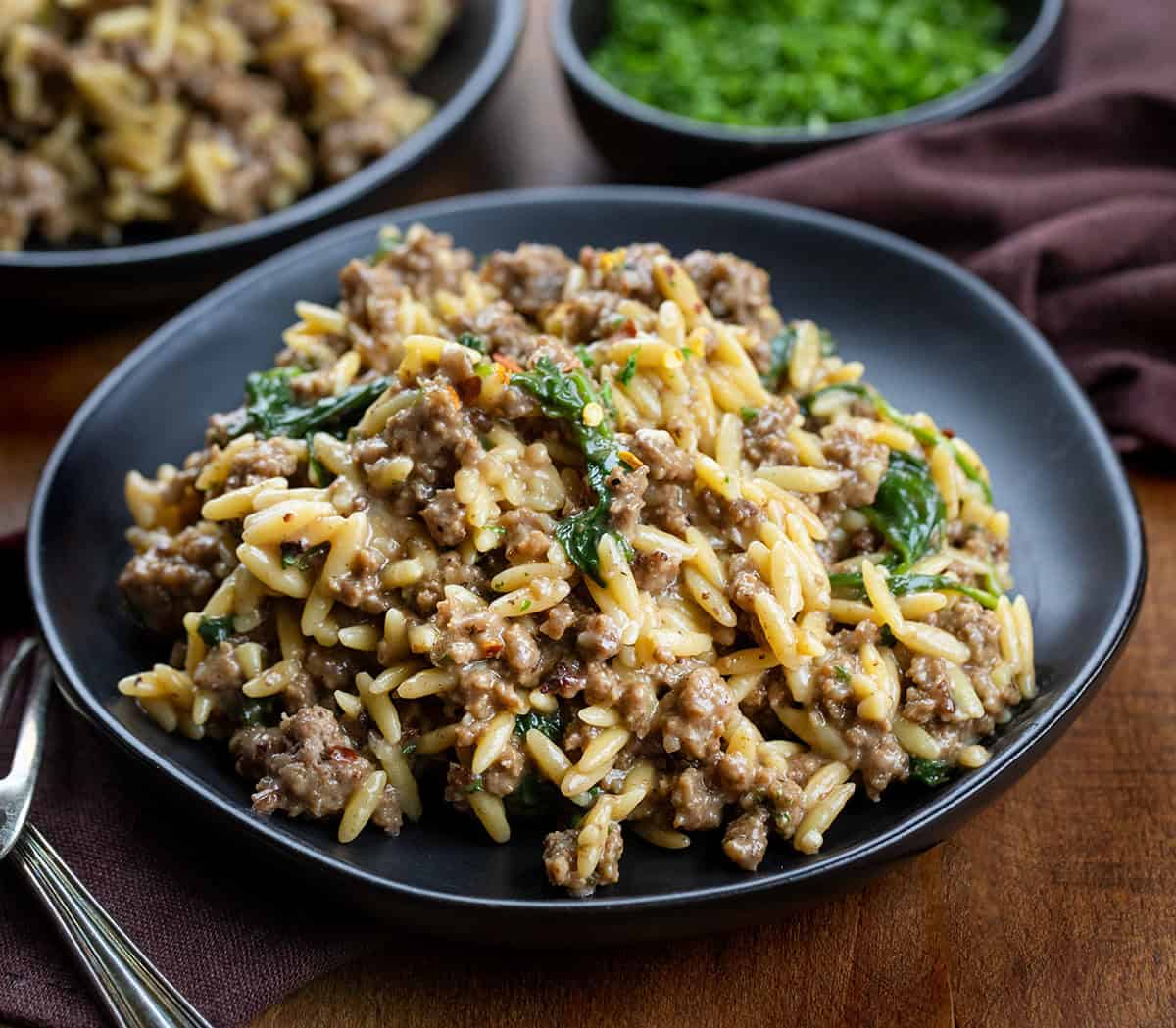 Black plates with Cheesy Beef Orzo on them on a wooden table.
