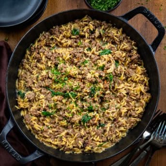 Skillet of Cheesy Beef Orzo on a wooden table from overhead.