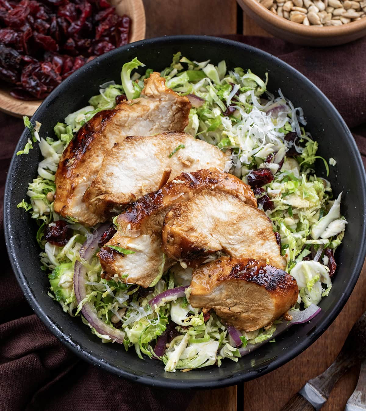 Black bowl with Chicken Brussels Sprout Salad in it on a wooden table from overhead.
