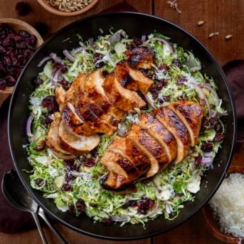 Black salad bowl filled with Chicken Brussels Sprout Salad on a wooden table from overhead.