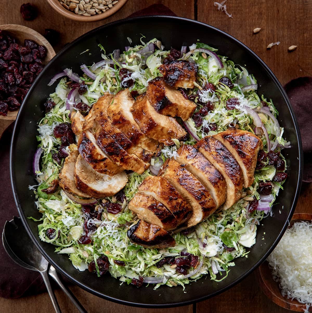 Black salad bowl filled with Chicken Brussels Sprout Salad on a wooden table from overhead.
