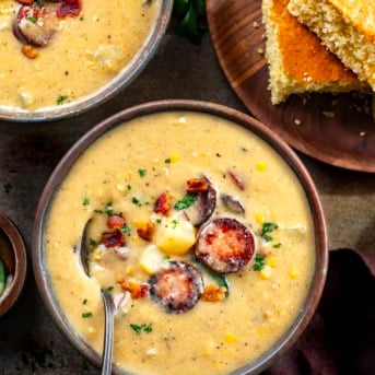 Bowls of Cowboy Corn Chowder one with a spoon in it on a wooden table with cornbread.
