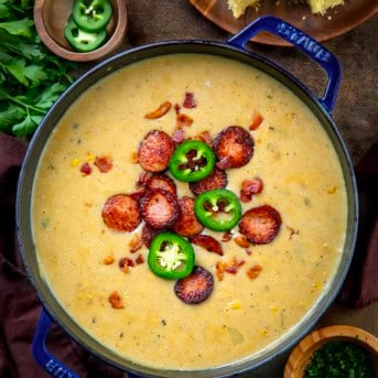 Pot of Cowboy Corn Chowder on a wooden table with cornbread and jalapeno.