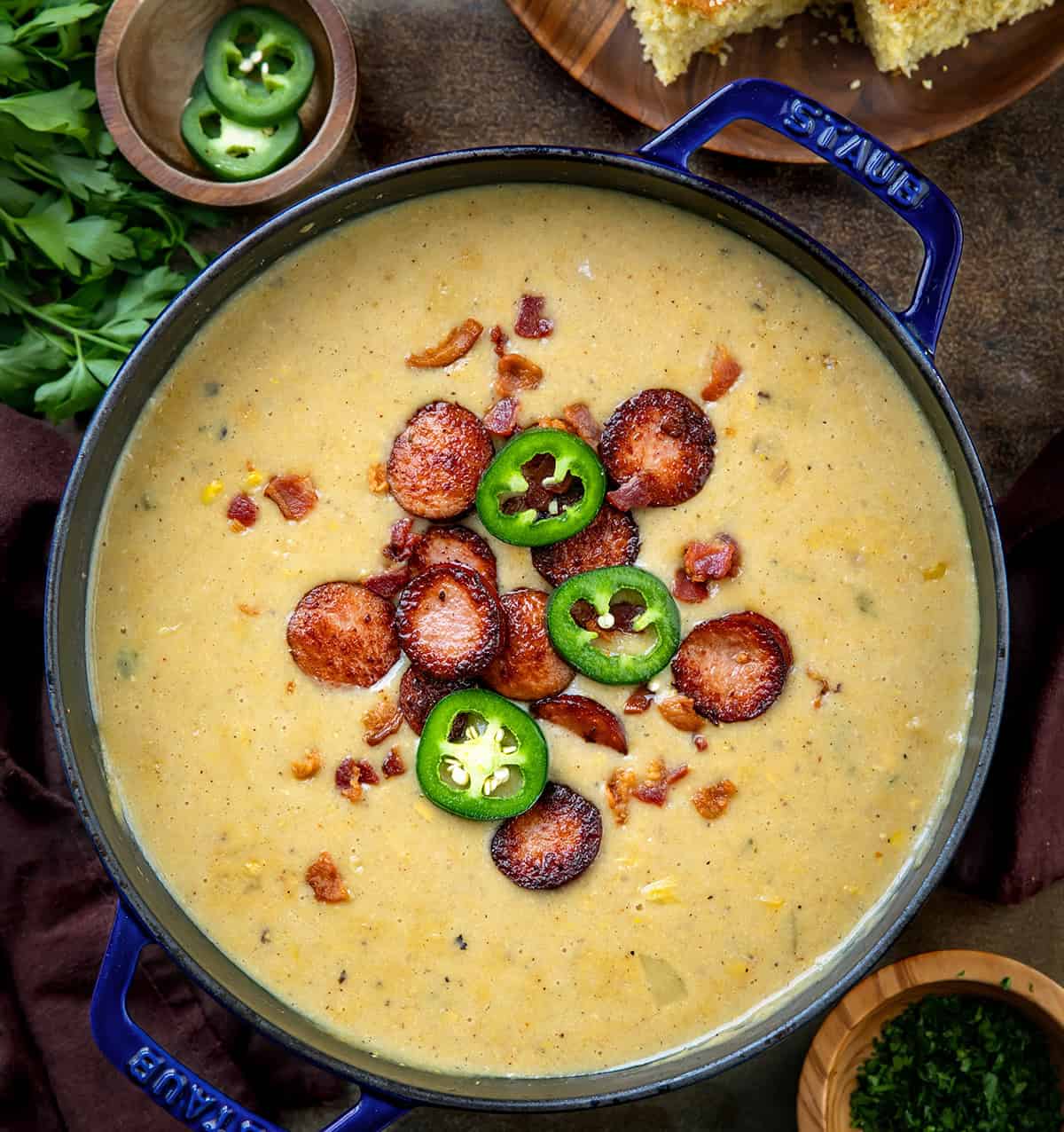 Pot of Cowboy Corn Chowder on a wooden table with cornbread and jalapeno.
