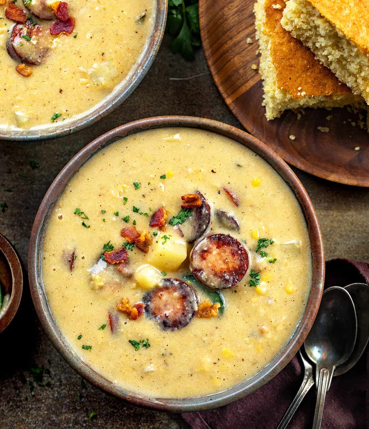 Bowls of Cowboy Corn Chowder on a wooden table with cornbread.