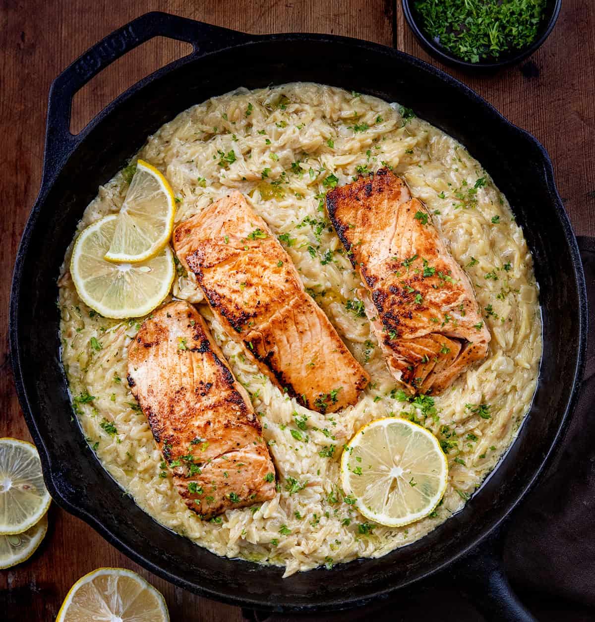Skillet of Creamy Lemon Orzo with Salmon on a wooden table from overhead. 