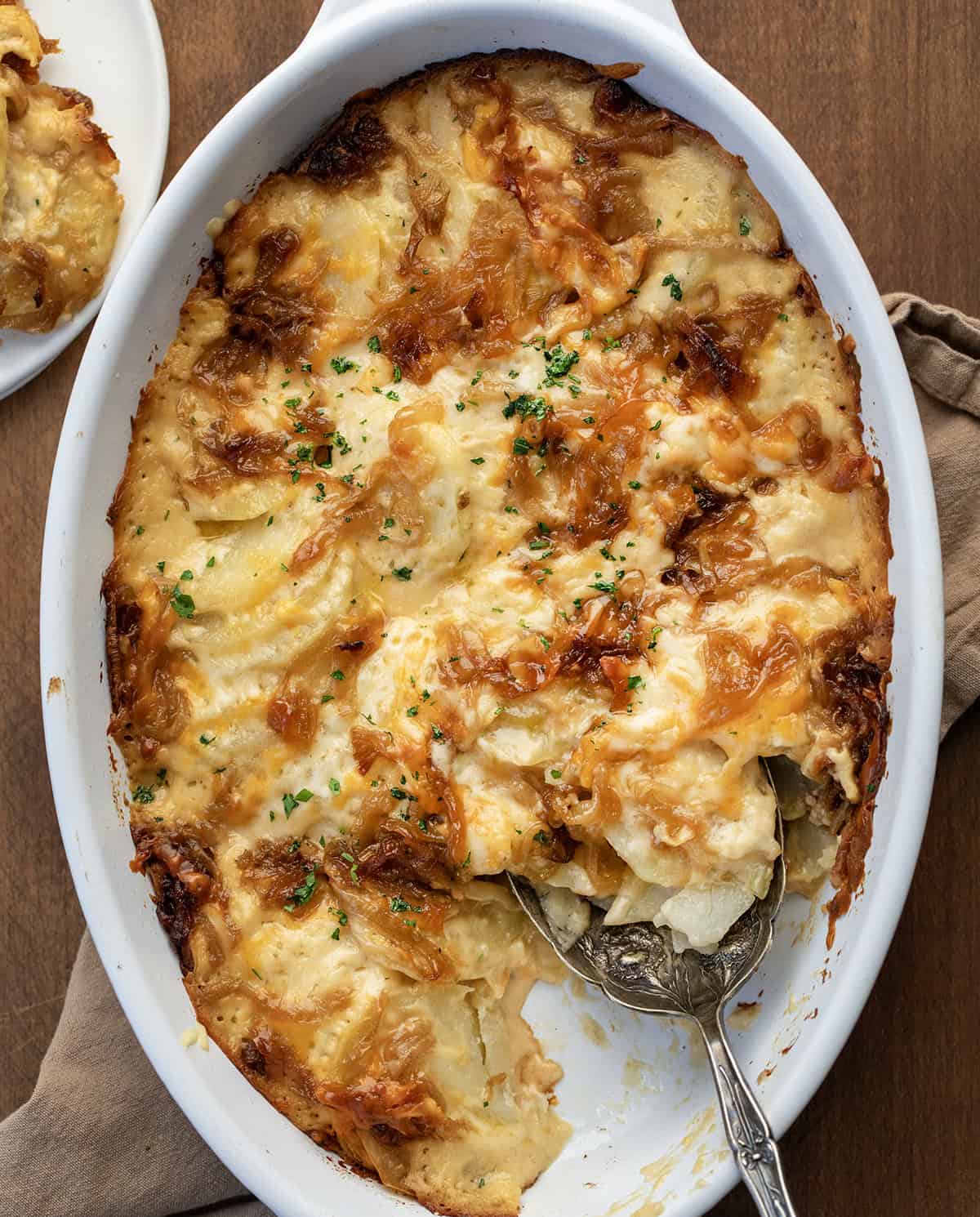 These Cheesy French Onion Scalloped Potatoes are rich, creamy, and loaded with caramelized onions and melty cheese! Dish of French Onion Scalloped Potatoes with some missing and a spoon resting in the dish.