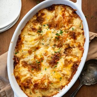 White dish filled with hot French Onion Scalloped Potatoes on a wooden table from overhead.