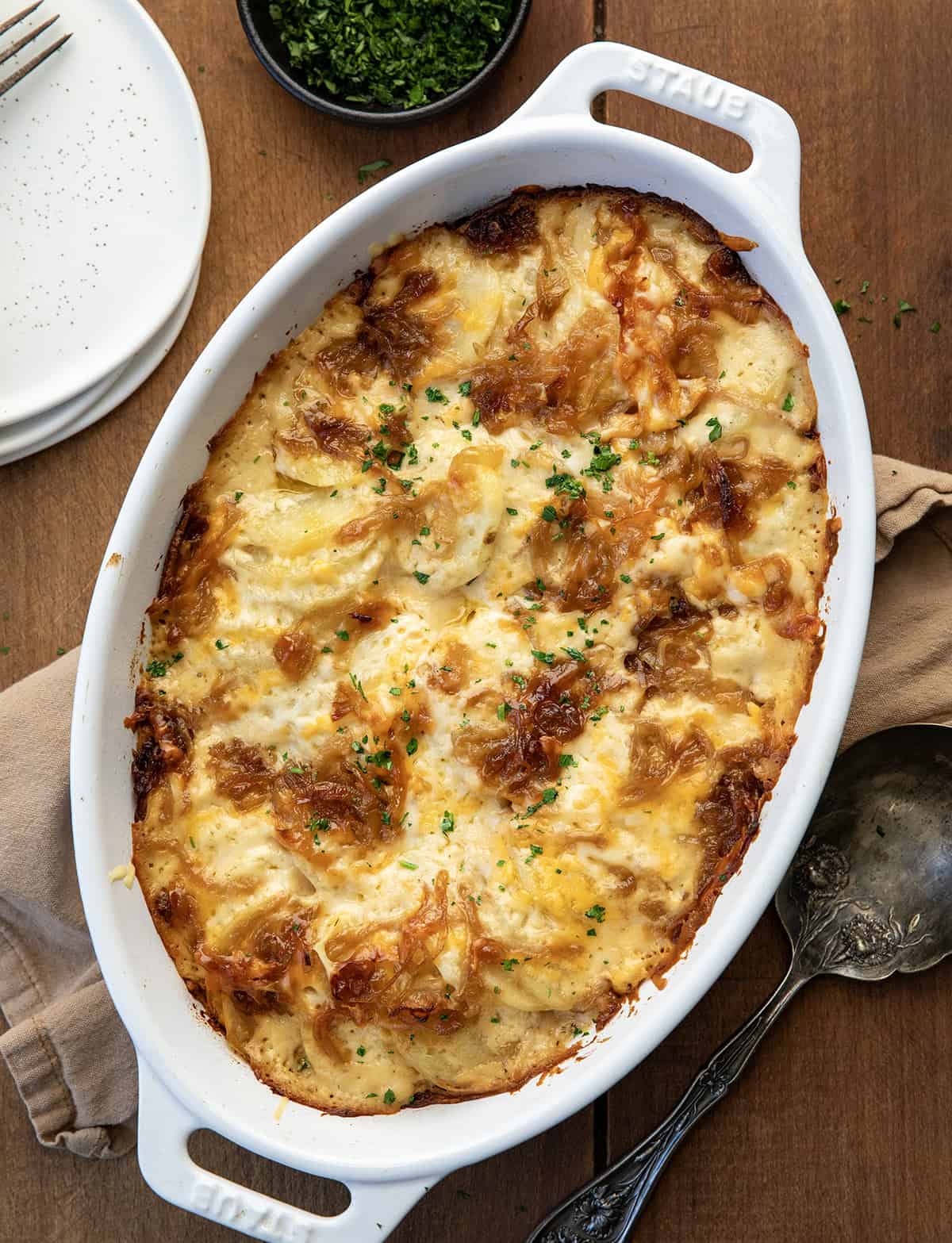 These Cheesy French Onion Scalloped Potatoes are rich, creamy, and loaded with caramelized onions and melty cheese! White dish filled with hot French Onion Scalloped Potatoes on a wooden table from overhead.