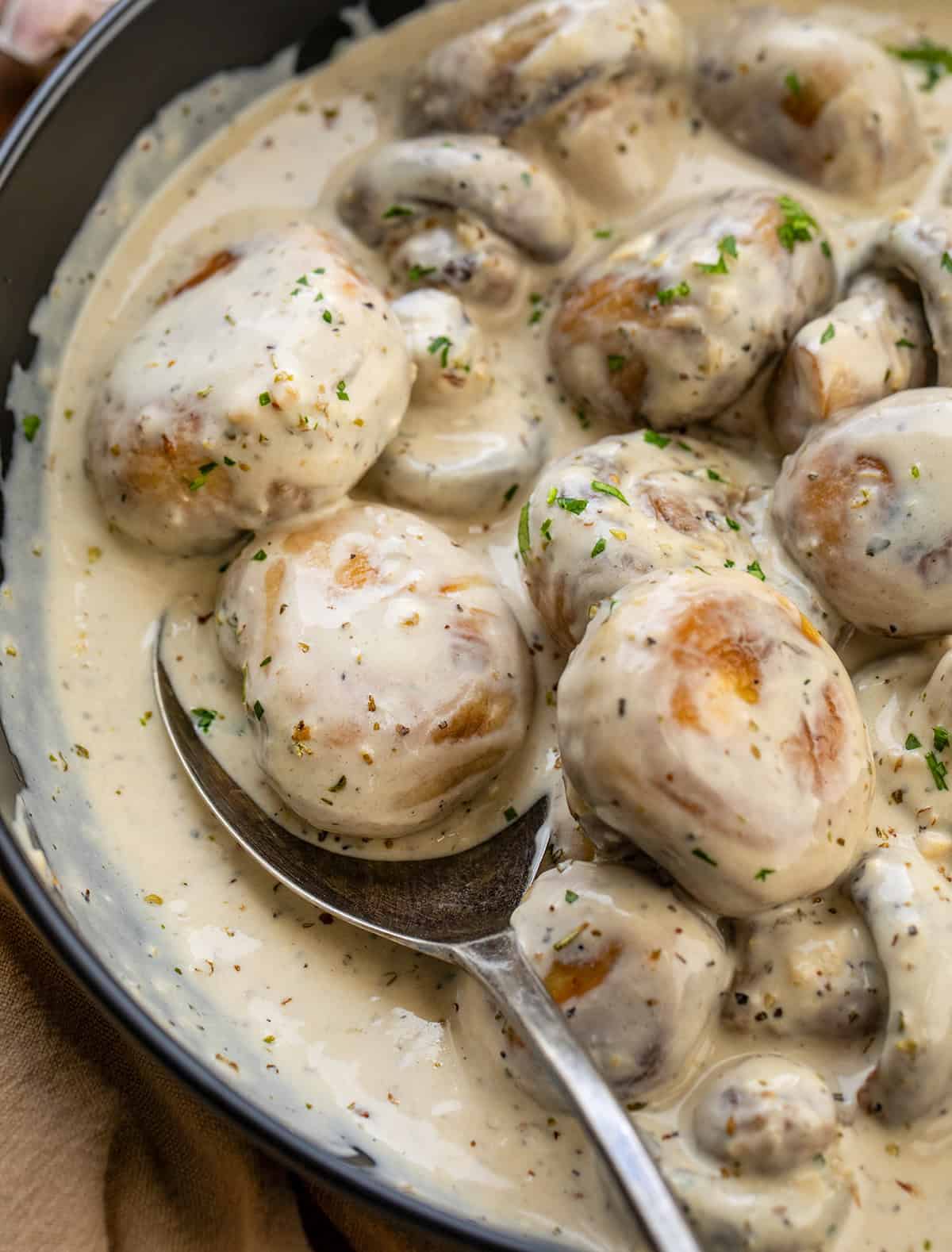 Spoon in a pan of Creamy Garlic Parmesan Mushrooms with a mushroom on it.