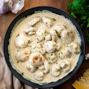 Black bowl of Creamy Garlic Parmesan Mushrooms on a wooden table from overhead.