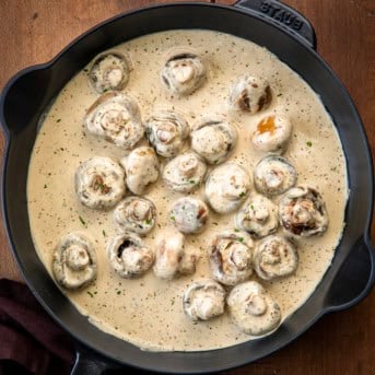 Black skillet of Creamy Garlic Parmesan Mushrooms on a wooden table from overhead.