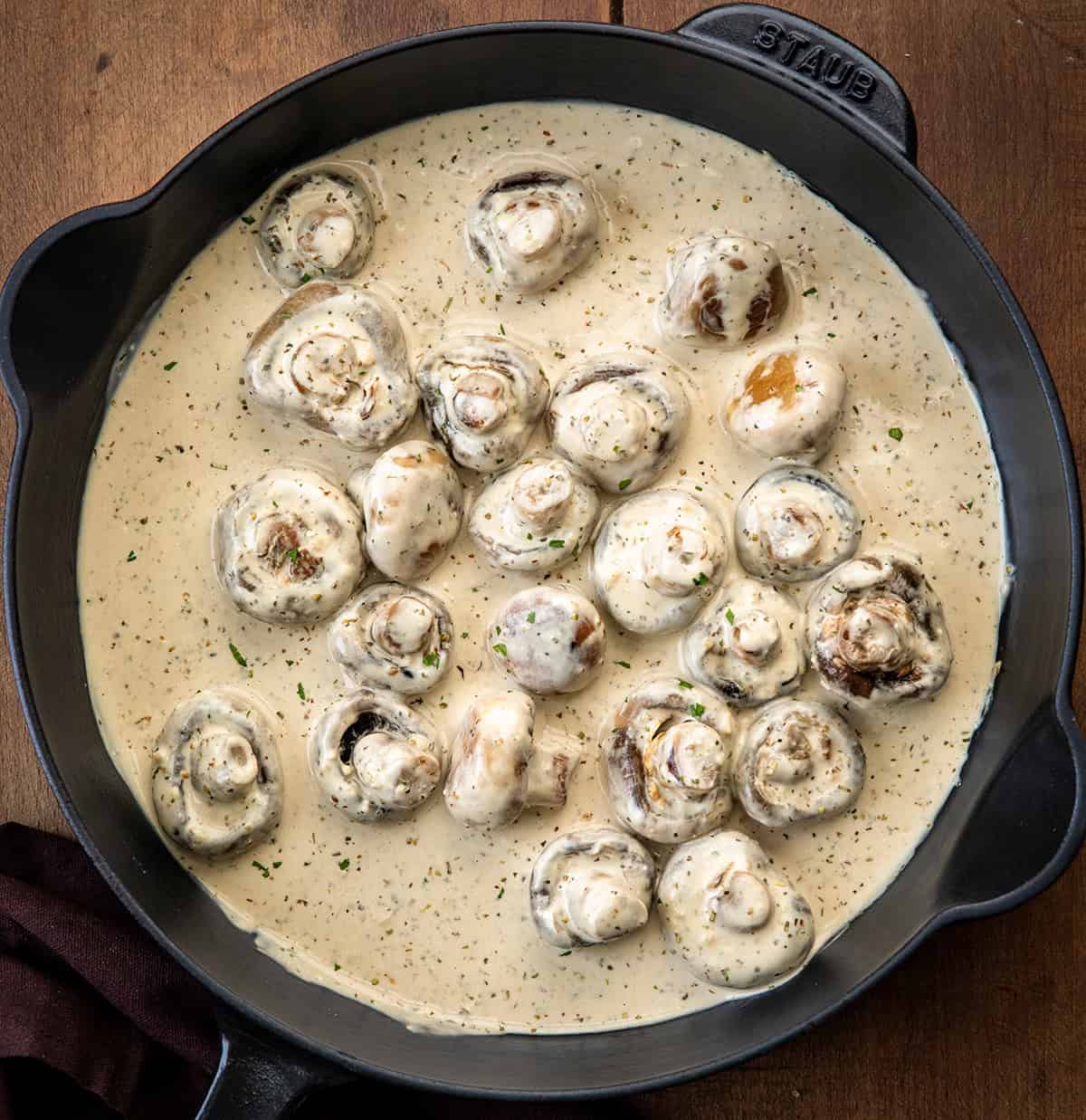 Black skillet of Creamy Garlic Parmesan Mushrooms on a wooden table from overhead.