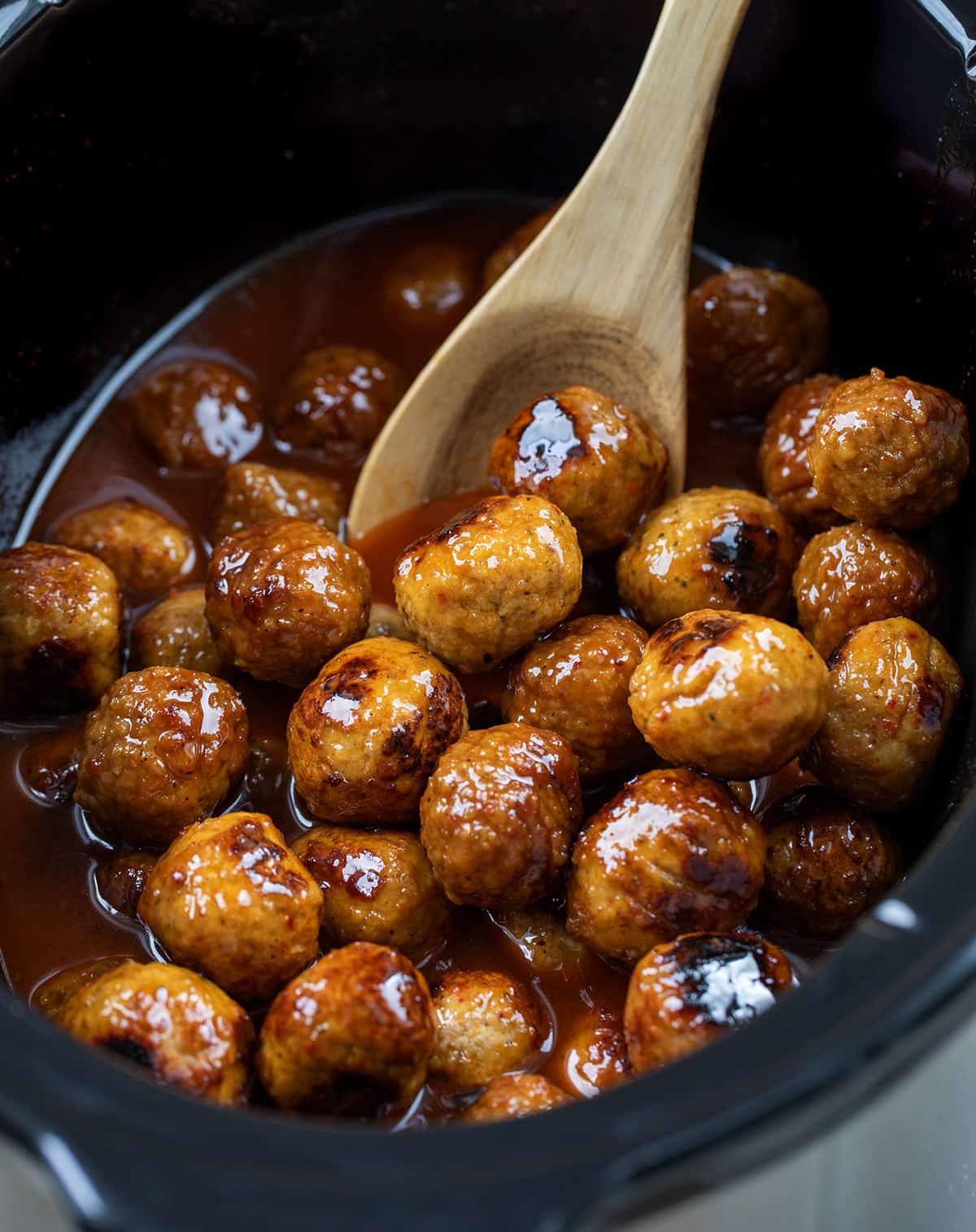 Wooden spoon in a slow cooker filled with Honey Buffalo Meatballs.