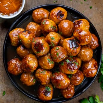 Black plate with Honey Buffalo Meatballs on it and a ramekin of honey from overhead.