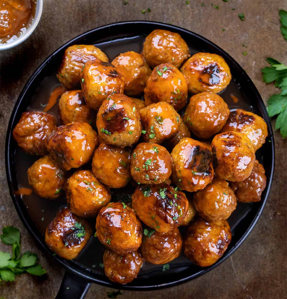 Black plate with Honey Buffalo Meatballs on it and a ramekin of honey from overhead.