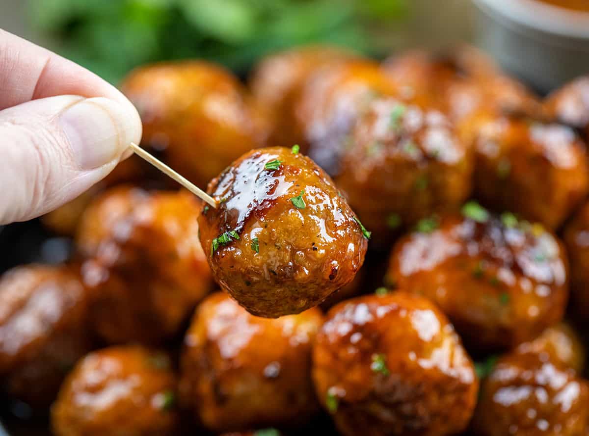 Hand holding a Honey Buffalo Meatball with a toothpick in it.