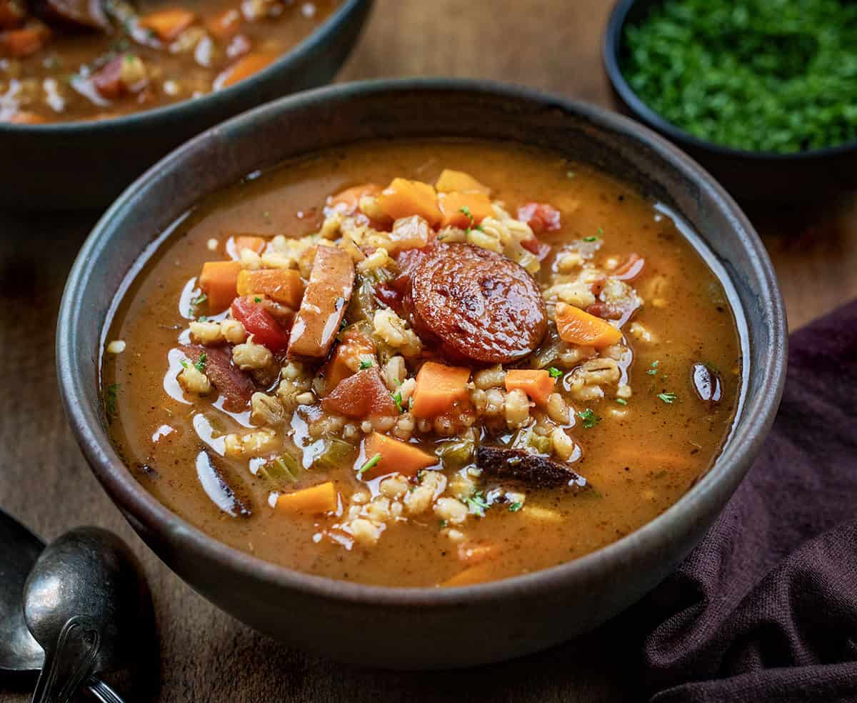 Close up of a bowl of Kielbasa Barley Soup on a wooden table.