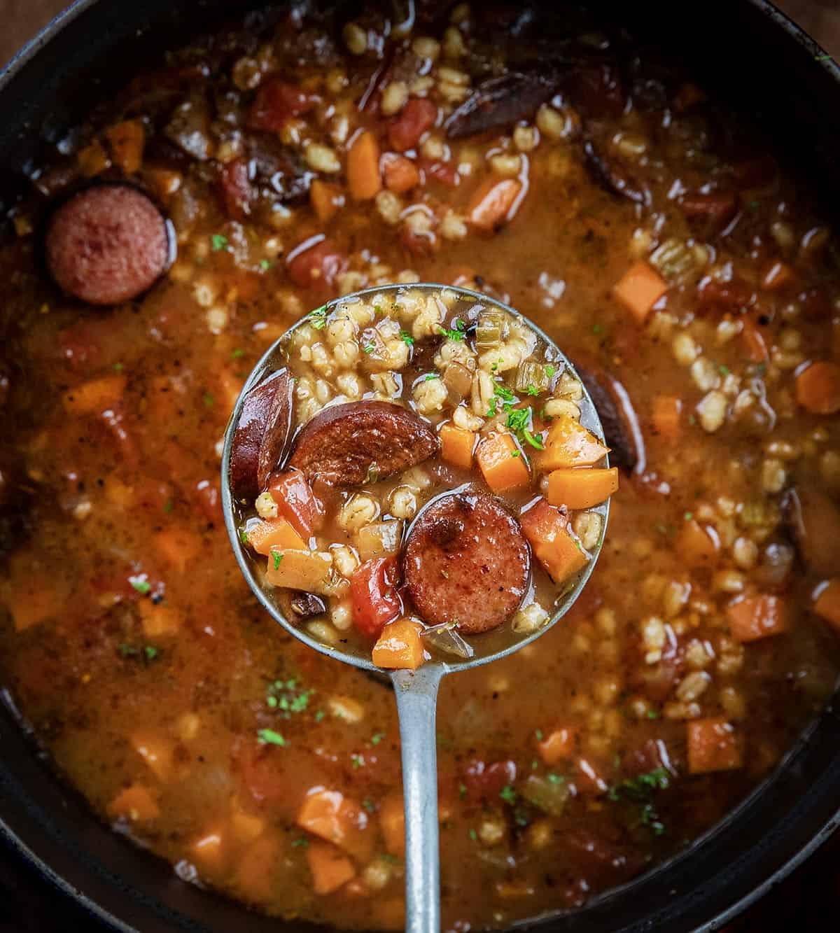 Ladle full of Kielbasa Barley Soup held above the pot.
