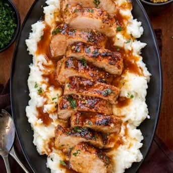 Sliced up Maple Dijon Pork Tenderloin on a bed of mashed potatoes on a black plate resting on a wooden table from overhead.