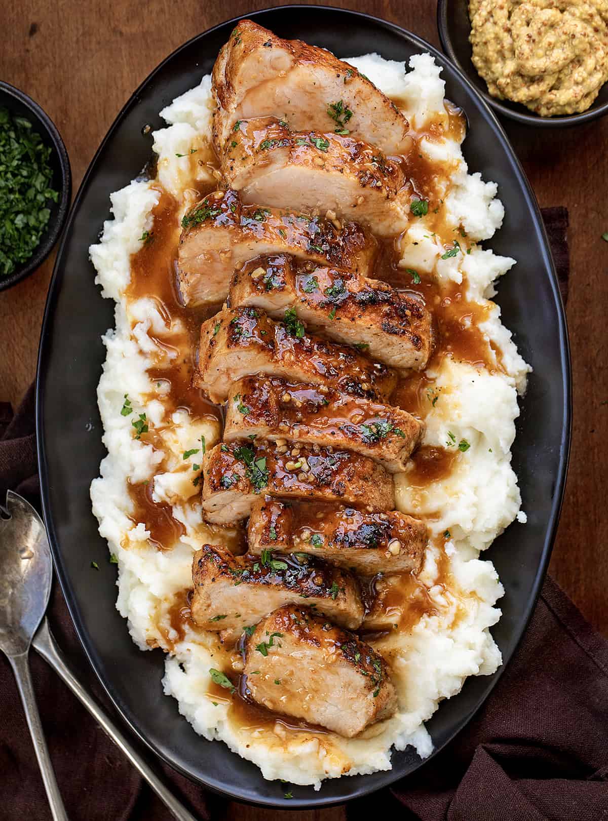 Sliced up Maple Dijon Pork Tenderloin on a bed of mashed potatoes on a black plate resting on a wooden table from overhead.