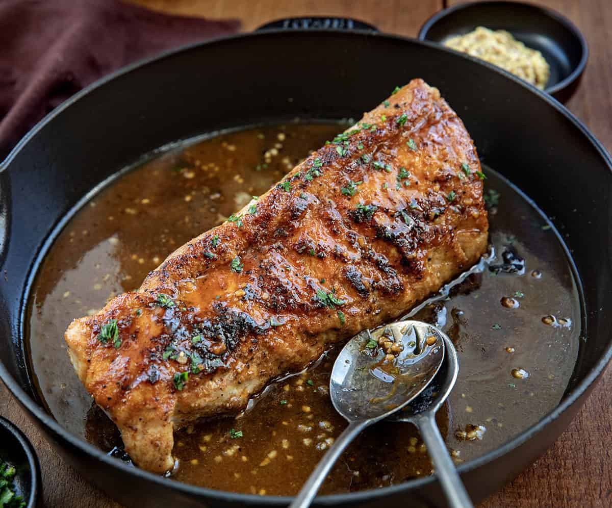 Maple Dijon Pork Tenderloin in a pan on a wooden table with spoons in the pan.