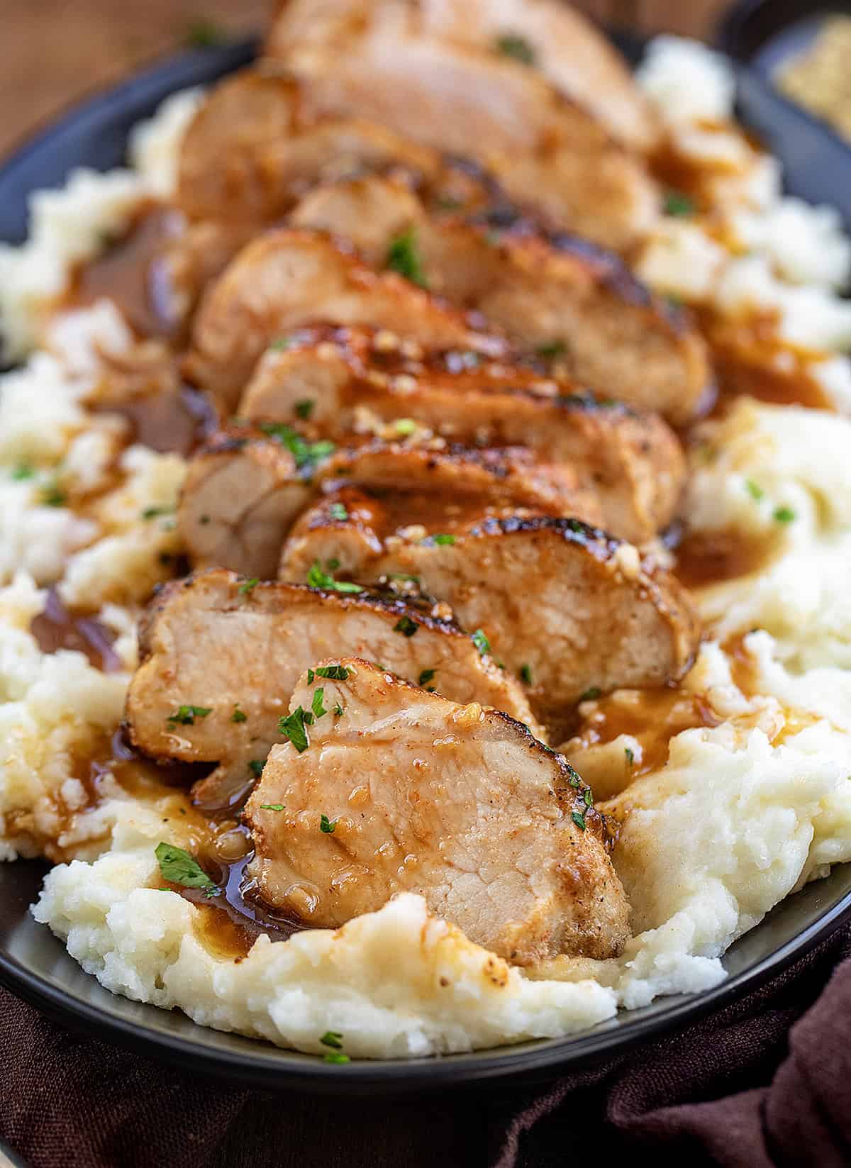 Sliced up Maple Dijon Pork Tenderloin on a bed of mashed potatoes close up.