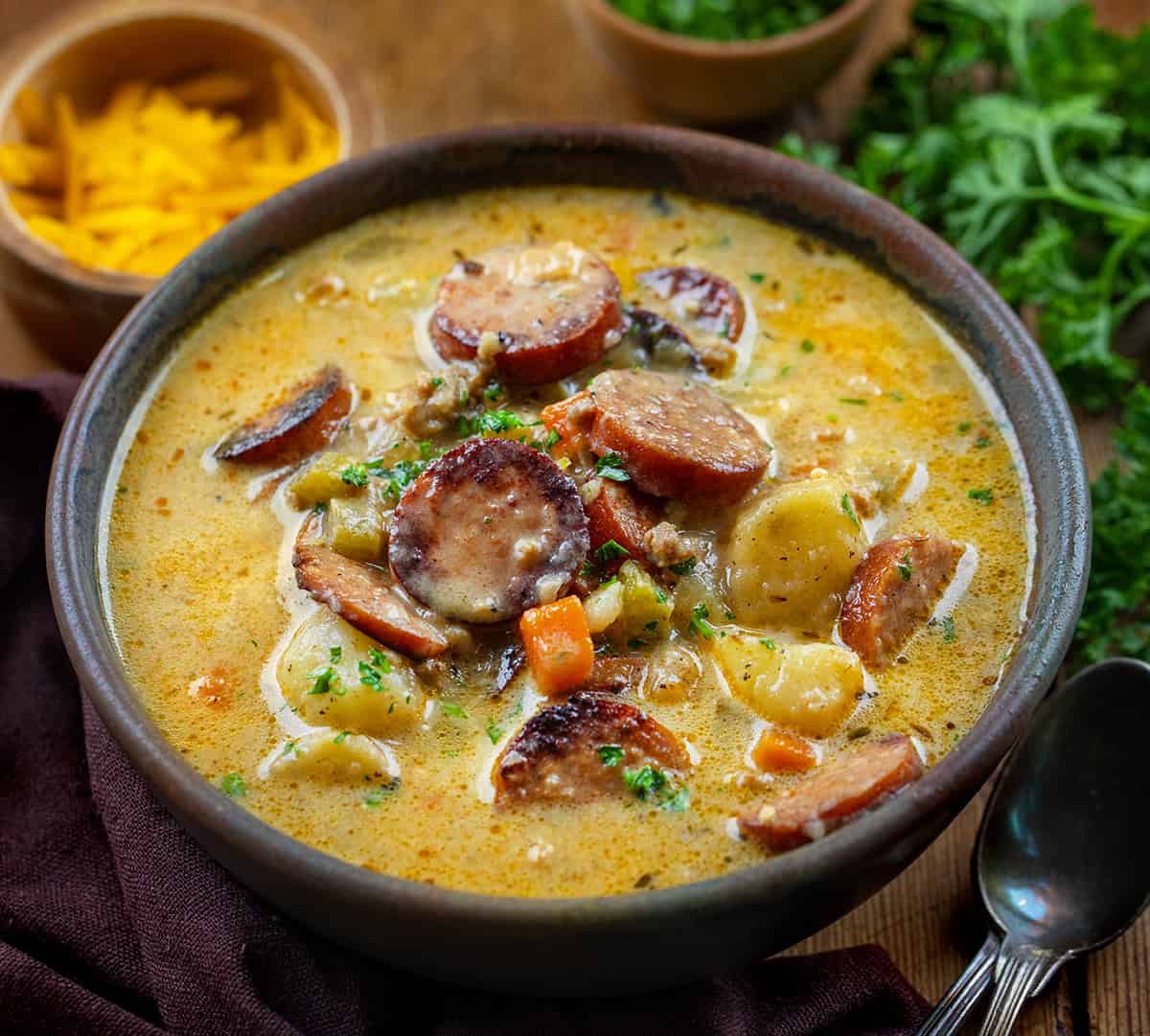 Bowl of Spicy Cajun Sausage Potato Soup on a wooden table with spoons and cheese.