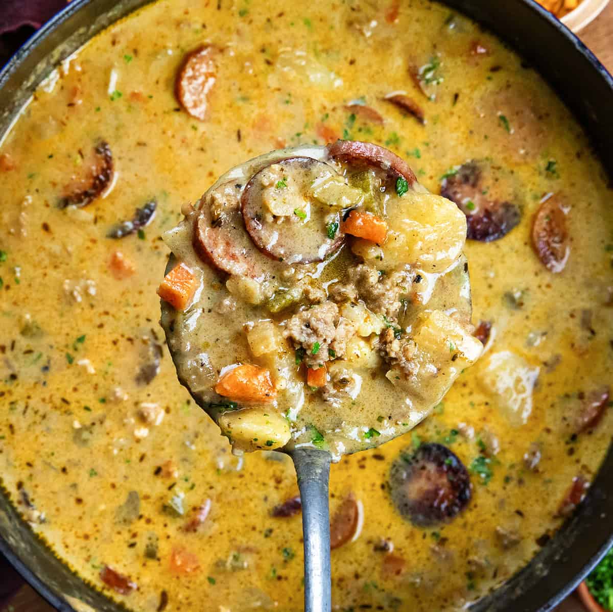 Ladle full of Spicy Cajun Sausage Potato Soup being held above the pot.