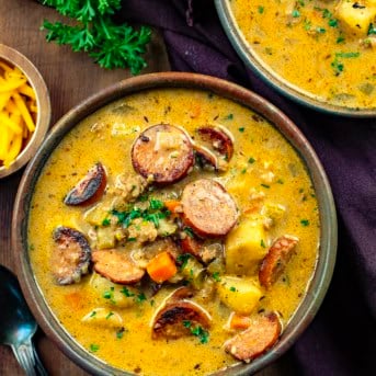 Bowls of Spicy Cajun Sausage Potato Soup on a wooden table with a brown napkin and spoons.