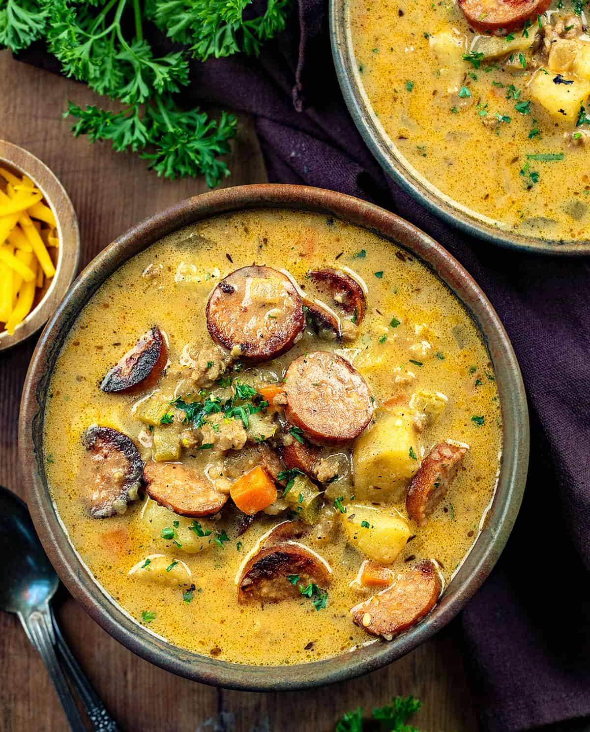 Bowls of Spicy Cajun Sausage Potato Soup on a wooden table with a brown napkin and spoons.