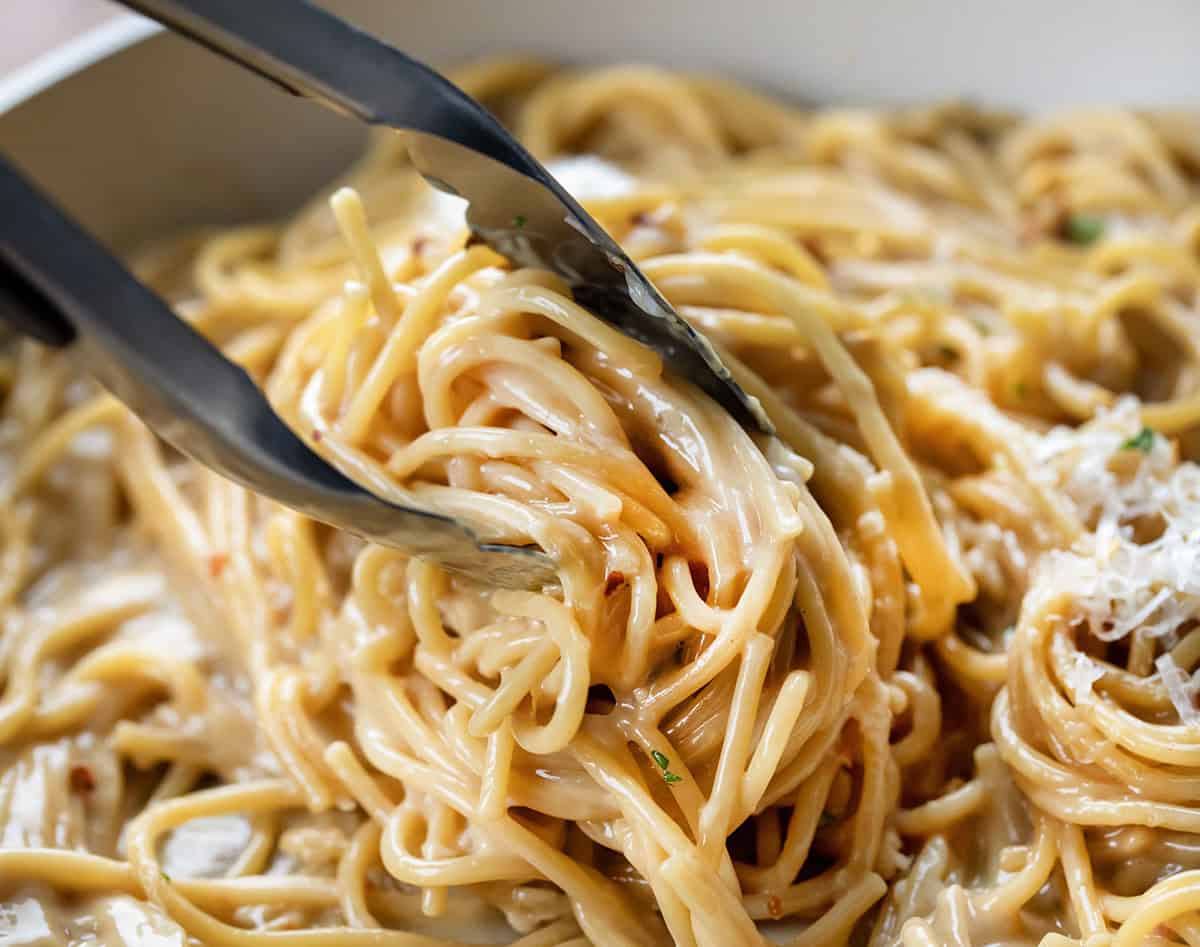 Tongs picking up a portion of ultra creamy Sticky Honey Garlic Pasta.