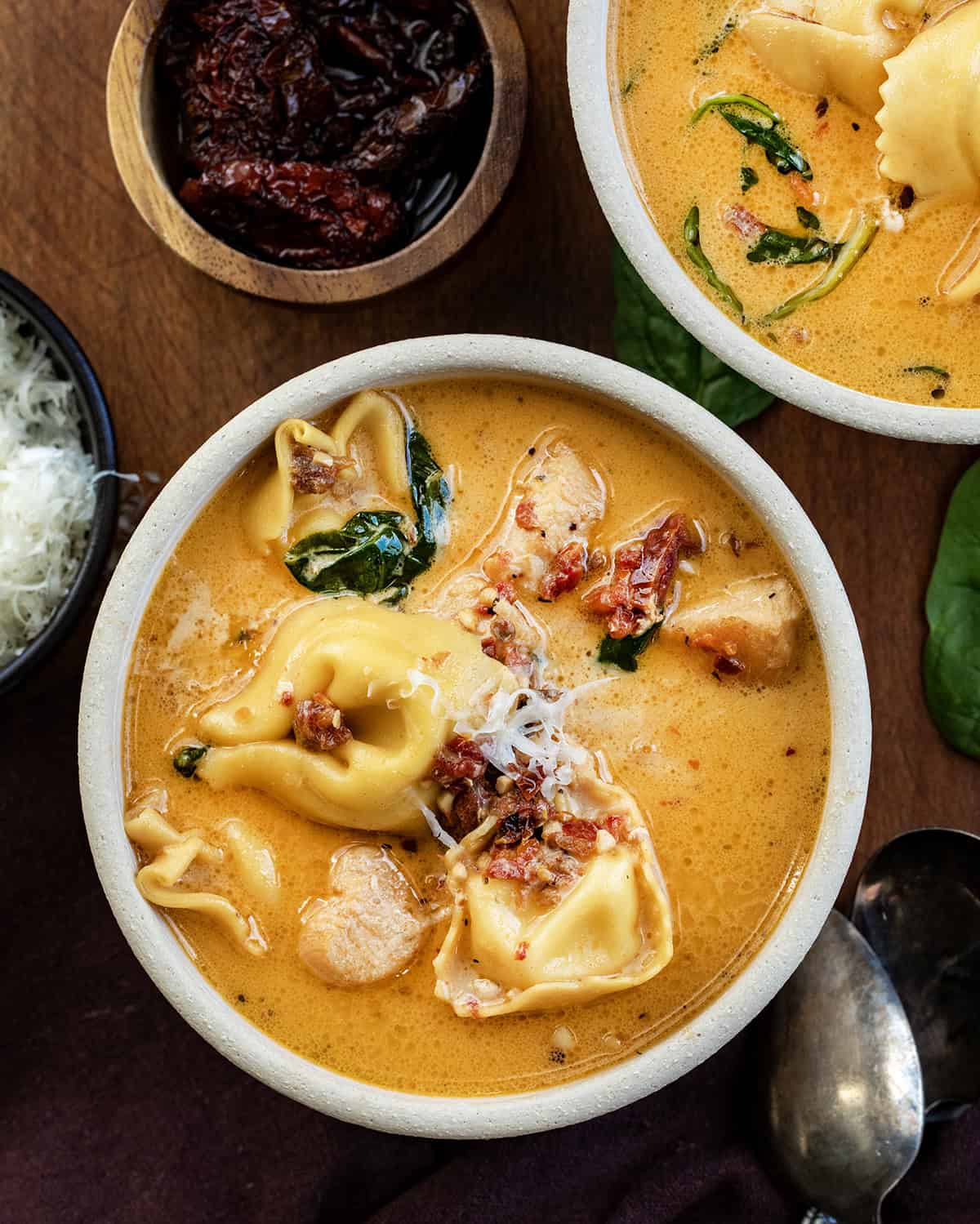 Bowls of Tuscan Chicken Tortellini Soup on a wooden table from overhead.